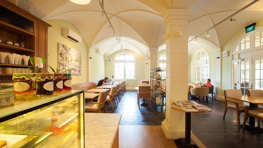 A cafe interior with tables and chairs, display shelves, and a long counter | The Shop | Central Mansions, Phnom Penh