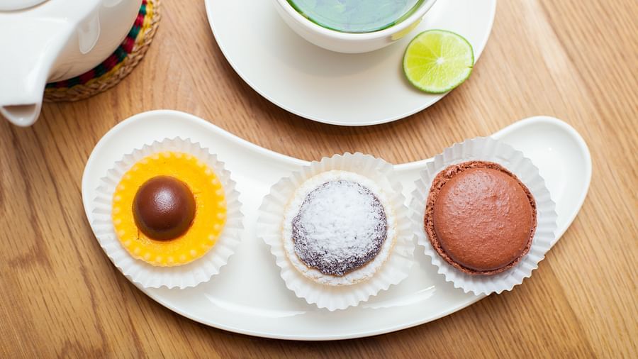 A top-down view of a white plate with three small desserts, placed next to a tea cup | The Shop | Central Mansions, Phnom Penh