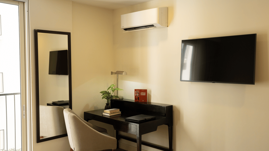 Bedroom workspace with a desk, chair, television, and wall mounted mirror at Central Mansions, Phnom Penh.