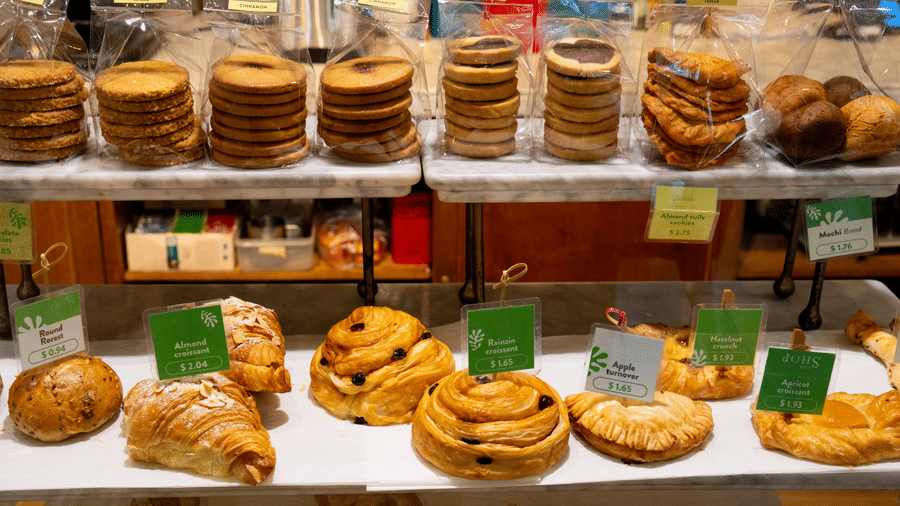 Bakery display featuring assorted cookies, croissants, pastries, and baked goods arranged on shelves.