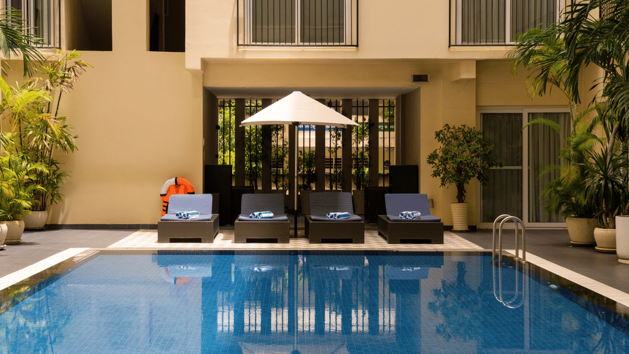 Outdoor swimming pool with lounge chairs, parasols, and surrounding accommodation buildings.
