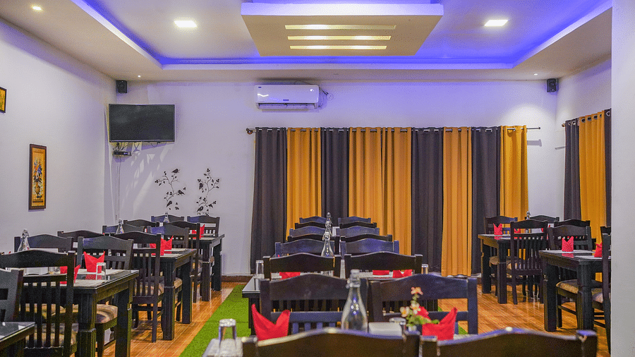 Image of a dining space with tables and chairs and a television mounted on the wall at Coorg Jungle Camp Backwater Resort, Kushalnagar.
