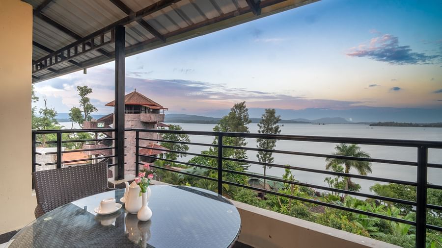 Image of a balcony with seating area overlooking a water body and plants surrounding it at Coorg Jungle Camp Backwater Resort, Kushalnagar.