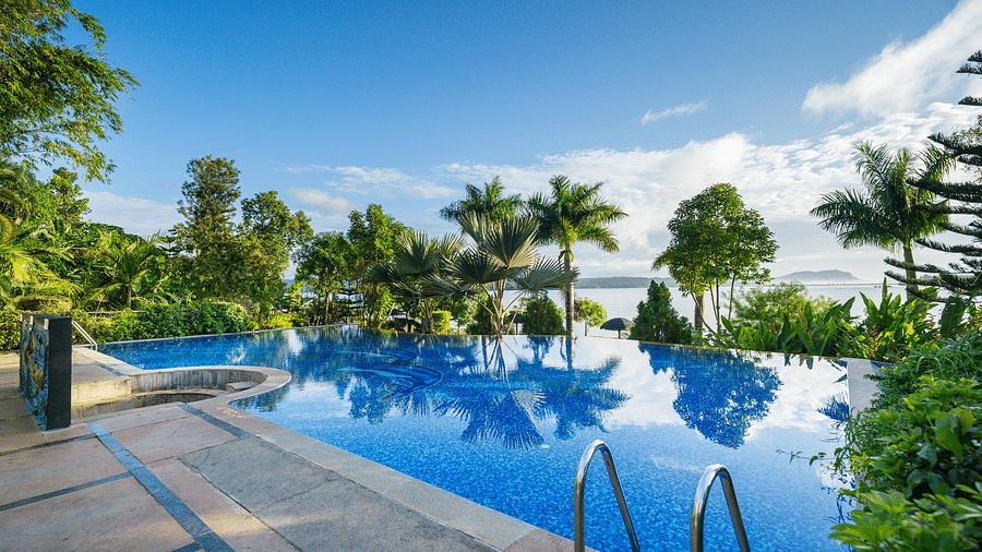 A swimming pool with trees surrounding it at Coorg Jungle Camp Backwater Resort, Kushalnagar.