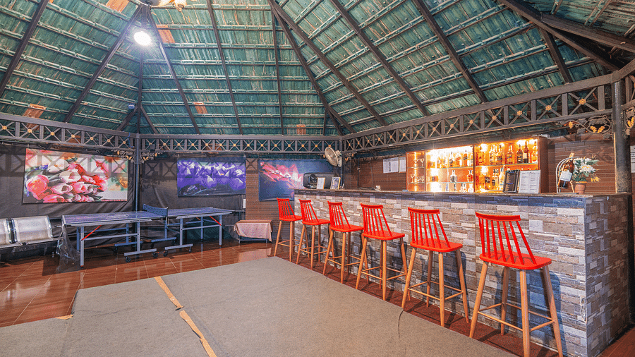 A bar with high chairs placed in front of the bar at Coorg Jungle Camp Backwater Resort, Kushalnagar.