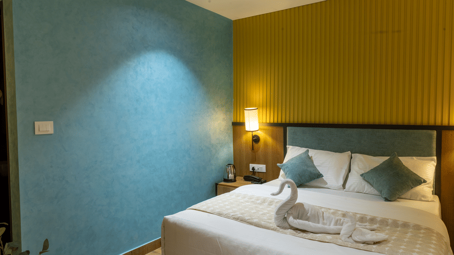 Stylish hotel bedroom showcasing a double bed set against a teal feature wall and warm yellow panelling.