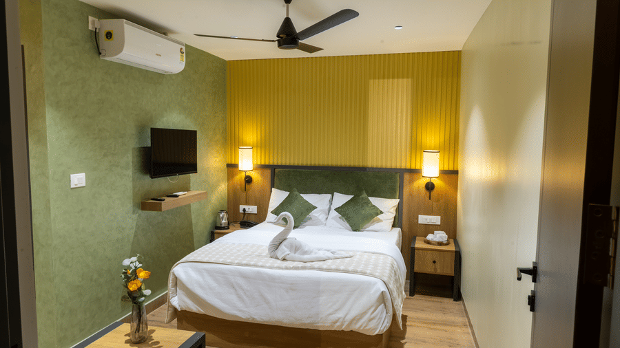 Full view of a hotel room with a neatly made double bed, ceiling fan, and wooden side table.