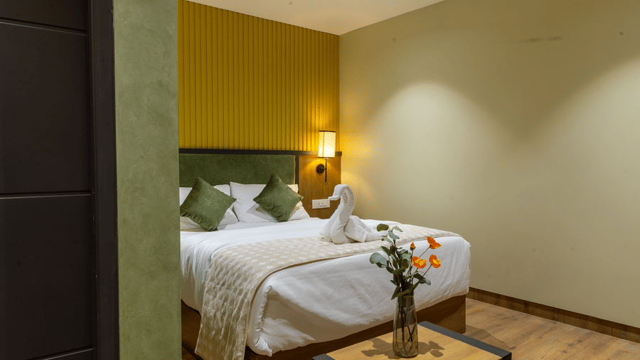 Entrance perspective of a hotel suite showing a wooden table with fresh flowers in front of a double bed.