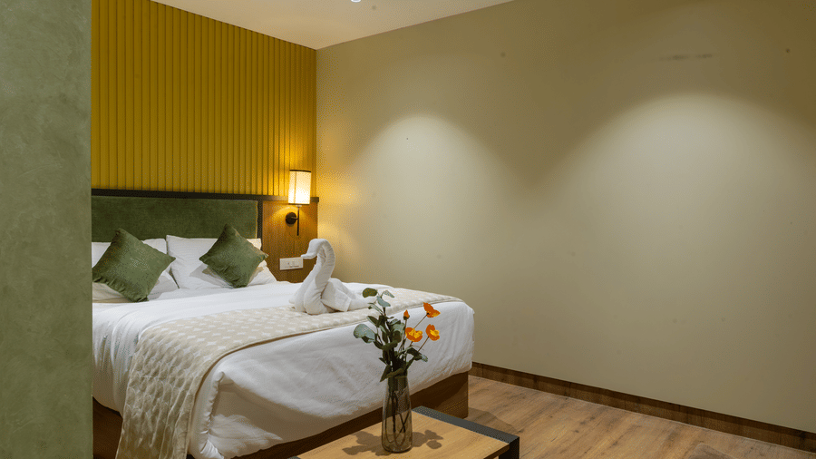 Elegantly styled hotel room with a bed, green cushions, bedside reading lamps, and warm wall decor.
