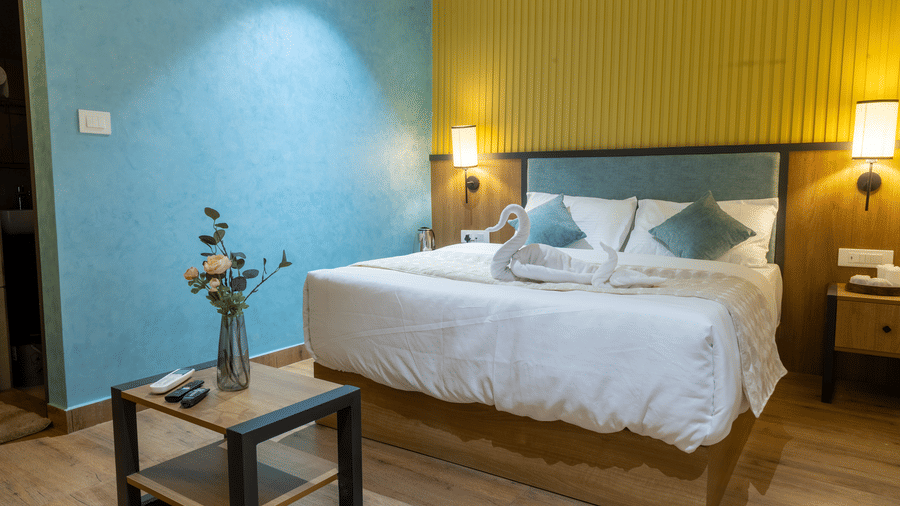 Angle view of a bedroom showcasing white bed linen, decorative swan towels, and a small side table.