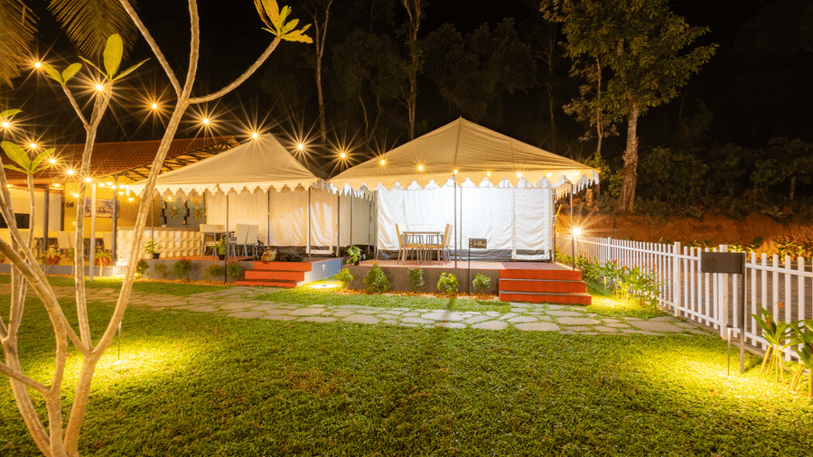 Nighttime view of luxury glamping tents surrounded by a manicured lawn and warm outdoor garden lights.