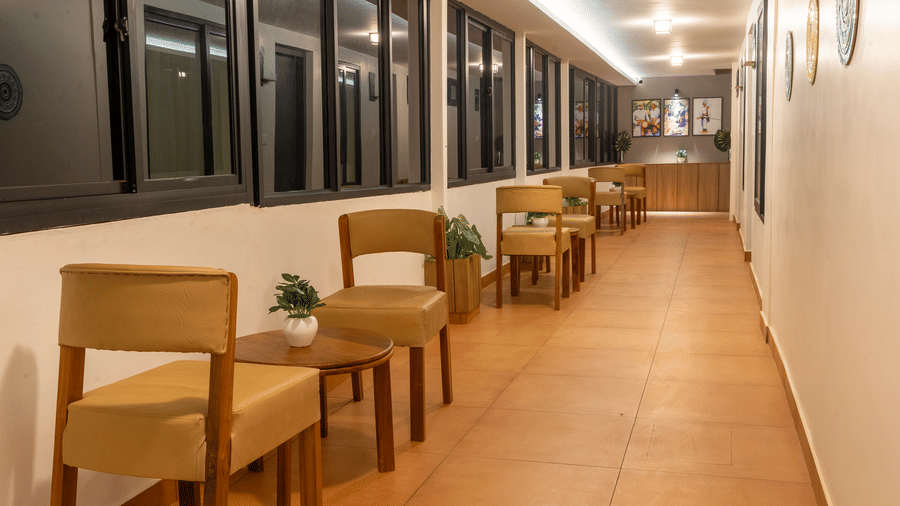 Long resort hallway lined with warm-toned wooden chairs, small tables, and large windows.