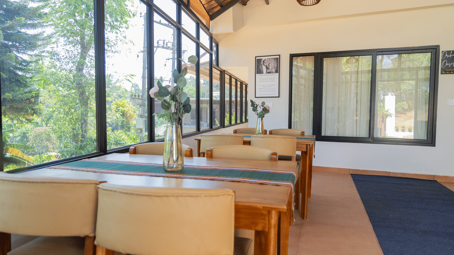 Bright resort dining space featuring large glass windows, green views, wooden tables, and neutral seating.