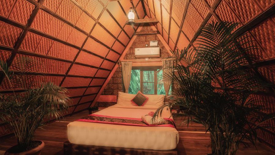 A bedroom at Copper Edge Eco Resort featuring attic style roof, a lamp hanging on the ceiling, a bed, AC, and some plants at the corner.