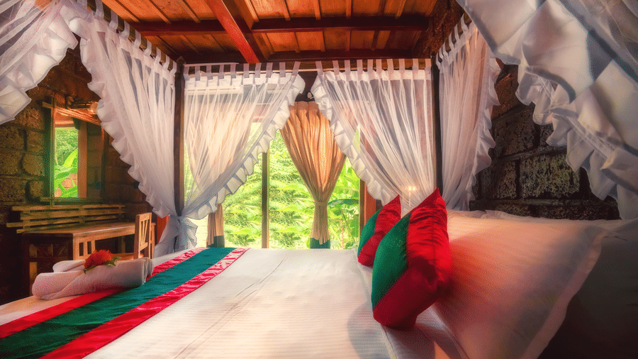Oak Jacuzzi Villa at Copper Edge, the best resort in Kodagu, featuring a plush bed with pillows, cushion, and bed runner next to a glass ceiling-to-floor window with greenery view