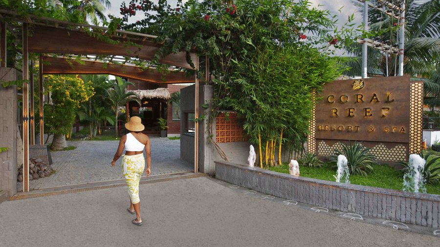 A woman walking towards the entrance of the Coral Reef Hotel & Resort wearing beachwear.
