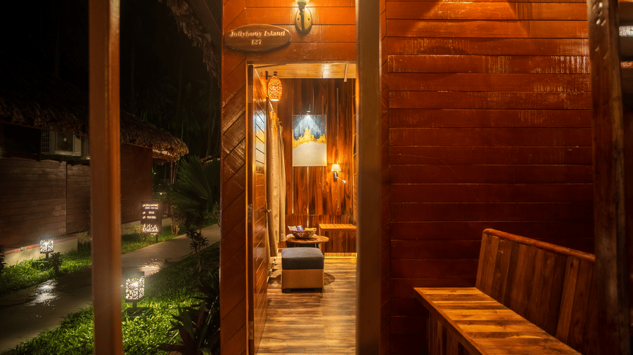 A view of an outdoor wooden seating area illuminated by soft lighting. The wooden structure and rustic design add a tranquil charm to the space.