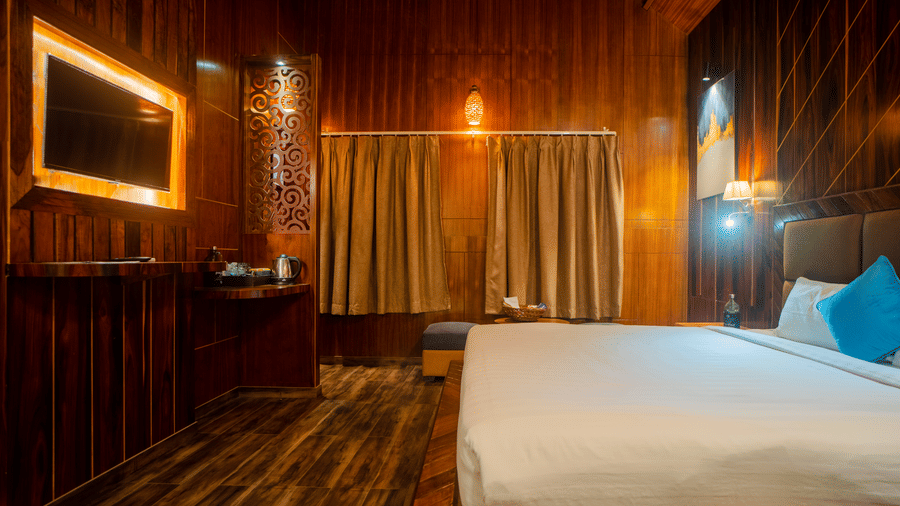 A view of a well-lit wooden hotel room, with soft lighting highlighting the bed and furniture. The warm tones and  design give the room a welcoming feel.