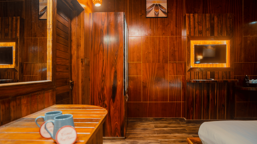 A warm, wooden room with a comfortable bed, stylish lamps, and soft ambient lighting. The simple yet elegant decor creates a peaceful atmosphere.