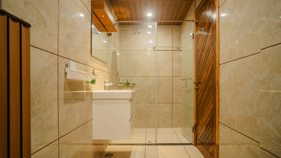 A modern bathroom with marble walls, a white sink, and a shower area. The clean design is complemented by bright lighting, giving the space a fresh and sleek look.