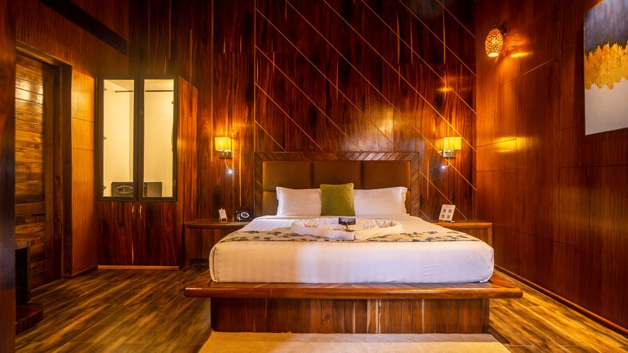  A stylish hotel room with a wooden interior, featuring a large bed, soft lighting, and comfortable seating. The room has a calm, rustic feel enhanced by the warm tones.