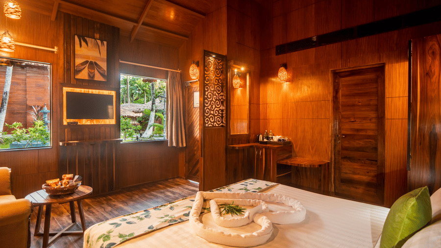 A detailed view of a wooden room with a king-sized bed, accent lighting, and modern amenities. The design is simple yet elegant, with wooden panels on the walls and floors.