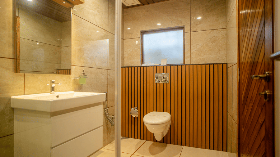 A modern bathroom with a white sink, toilet, and wooden paneling. The space is sleek and contemporary, with soft lighting that enhances the relaxed vibe.
