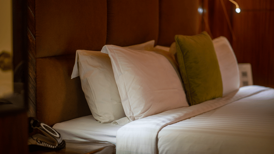 A close-up of a bed with white linens and green accent pillows. The room's wooden features and soft lighting create a welcoming, serene atmosphere.