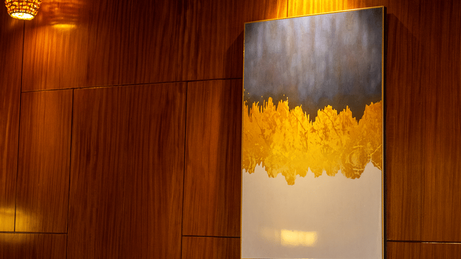 A modern artwork featuring soft yellow and white hues, hanging on a wooden wall. The ambient lighting adds a warm glow, complementing the room's rustic charm.