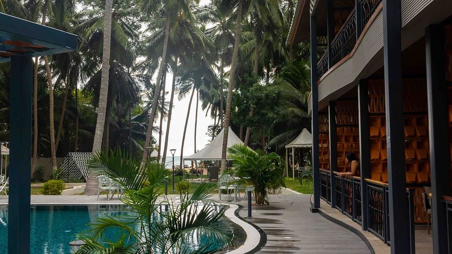A view of a modern pool area with tropical palm trees surrounding the space. The architecture of the building is visible, providing a relaxing and elegant setting - Coral Reef Resort & Spa, Havelock