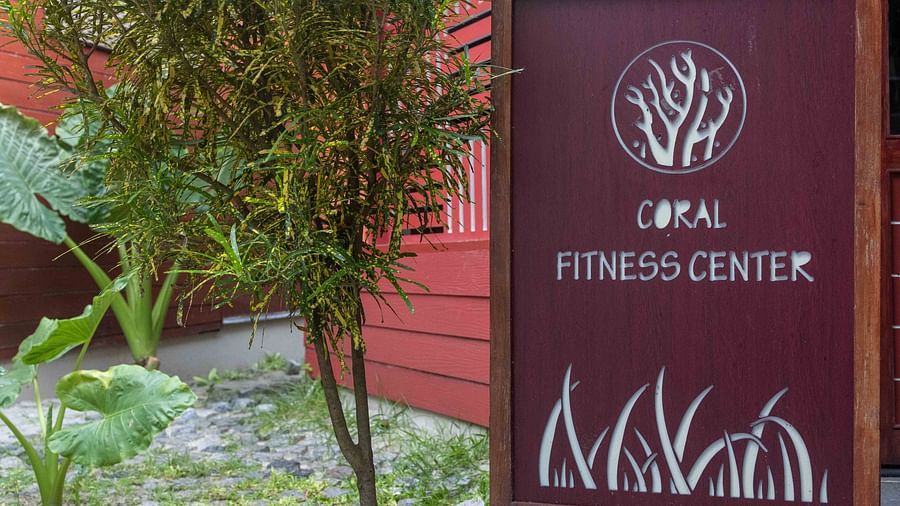 A sign for the Coral Fitness Center featuring sleek, modern design elements and a tree logo. The sign is set against a vibrant green garden, conveying a healthy and refreshing vibe - Coral Reef Resort & Spa, Havelock
