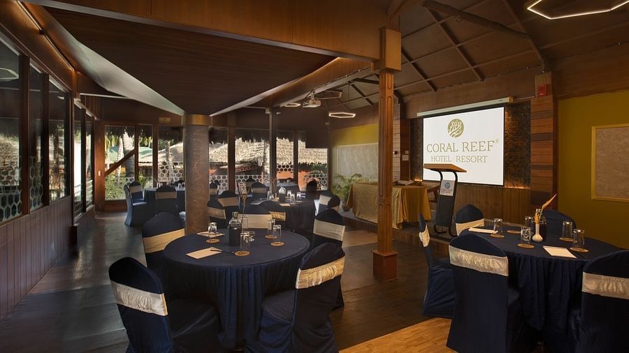 A modern, elegantly set-up banquet hall featuring dark blue table cloths and chairs, with a screen in the background for presentations. The room is well-lit with contemporary lighting - Coral Reef Resort & Spa, Havelock