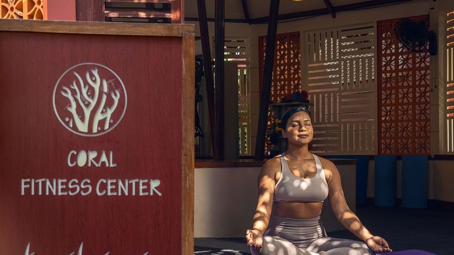 : A sign for the  Opal Fitness Center displayed alongside a statue of a person in a meditative pose. The background includes rustic wooden elements and a calm environment - Coral Reef Resort & Spa, Havelock