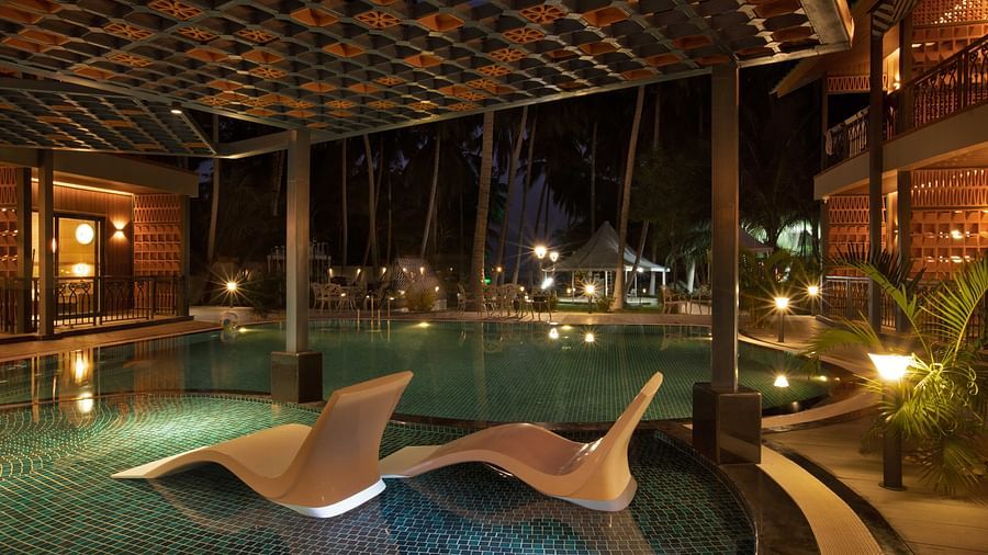 A tranquil outdoor pool area at dusk, with illuminated seating areas and palm trees surrounding the pool. The space has a peaceful, tropical atmosphere - Coral Reef Resort & Spa, Havelock