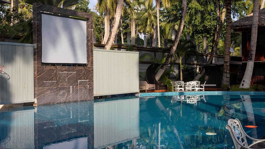 A poolside area with a large screen set up for an outdoor movie viewing at Splash Pool Bar. The pool is surrounded by lounge chairs, and palm trees provide a tropical backdrop - Coral Reef Resort & Spa, Havelock