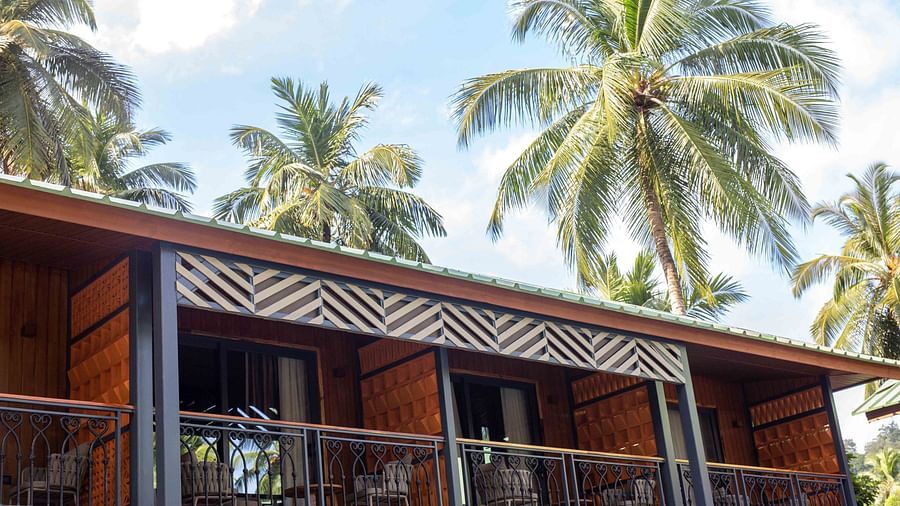 A view of a modern building with large windows, surrounded by palm trees and lush greenery. The design combines natural elements with contemporary architecture - Coral Reef Resort & Spa, Havelock