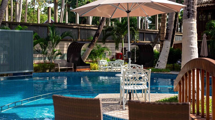 A pool area surrounded by tropical palm trees, with comfortable seating and a parasol at Splash Pool Bar. The tranquil setting offers a perfect space for relaxation - Coral Reef Resort & Spa, Havelock
