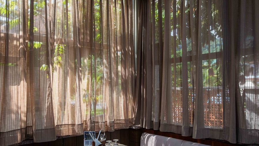 An indoor dining area at Ocean Prime Coral Reef Resort & Spa, Havelock with a wide sofa, a marble table, two glasses kept upside down on them and natural light coming through brown transparent curtains - Coral Reef Resort & Spa, Havelock