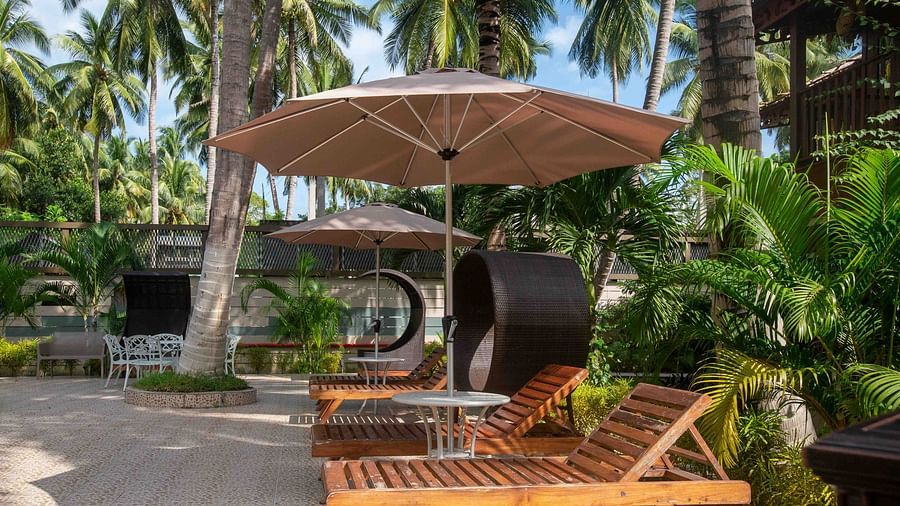   sun lounger placed under a shaded canopy, surrounded by palm trees and tropical greenery. The peaceful outdoor setting is perfect for relaxation - Coral Reef Resort & Spa, Havelock