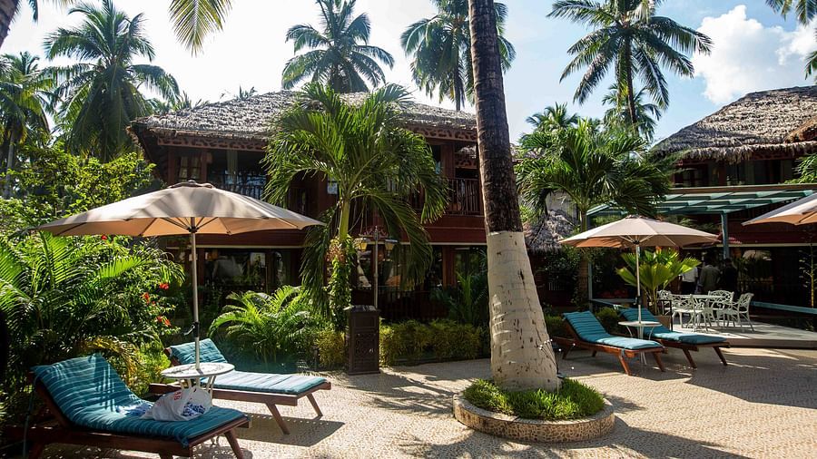 A resort garden with palm trees and sun loungers by the pool. The space is well-maintained, with umbrellas providing shade and a tranquil ambience - Coral Reef Resort & Spa, Havelock