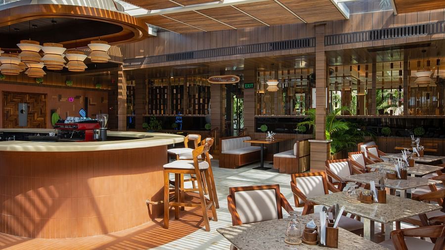 5th Bistro Cafe featuring a beautifully designed interior and dining area with wooden tables and chairs, suspended lighting fixtures, and tropical greenery. The space has a relaxed, elegant atmosphere - Coral Reef Resort & Spa, Havelock