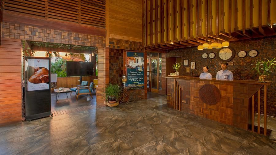 A spacious reception area featuring wooden accents with two people standing behind a wooden desk offering a seamless blend of rustic and modern elements. Large entrance letting in natural light, and the setting is calm and inviting - Coral Reef Resort & Sp