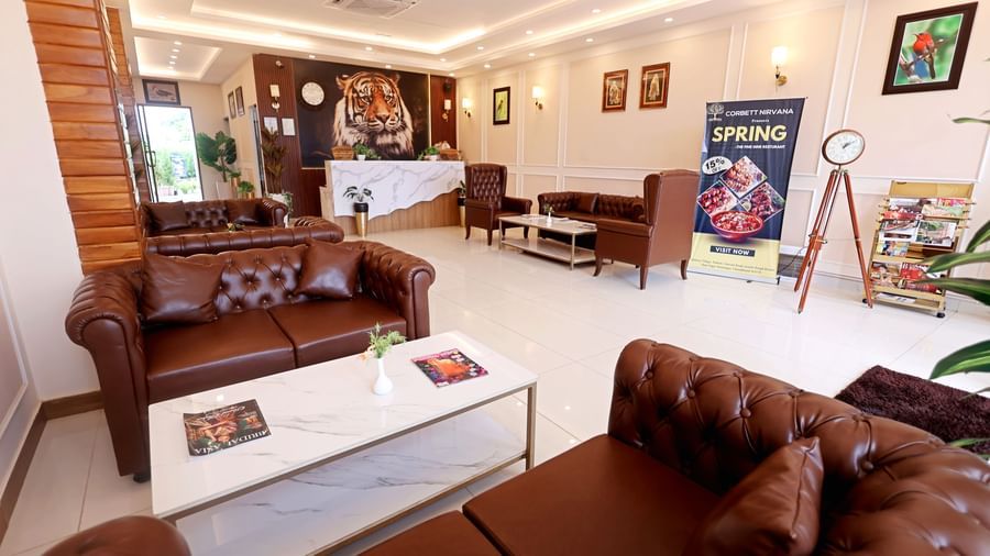 A cosy living area with comfortable brown leather sofas and colourful art on the walls at Corbett Nirvana Resort.