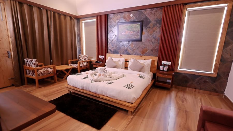 055A9205aLuxury bedroom with king-size bed, wooden flooring, and cosy seating at Corbett Nirvana Resort.