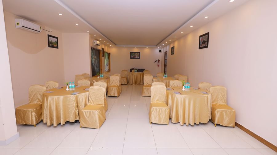 An empty banquet hall set up with tables and chairs draped in white and yellow linen at Corbett Nirvana Resort.