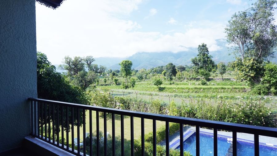 Balcony with railing overlooking lush greenery and pool at Corbett Nirvana Resort.