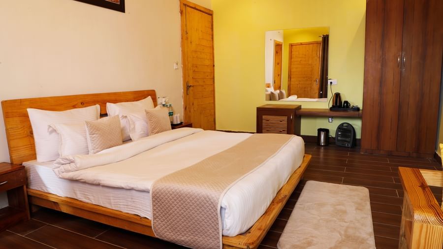 Spacious resort bedroom with a large bed, wooden flooring, and modern furnishings at Corbett Nirvana Resort.