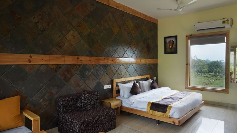 Elegant resort room with stone wall design, bed, and comfortable seating at Corbett Nirvana Resort.
