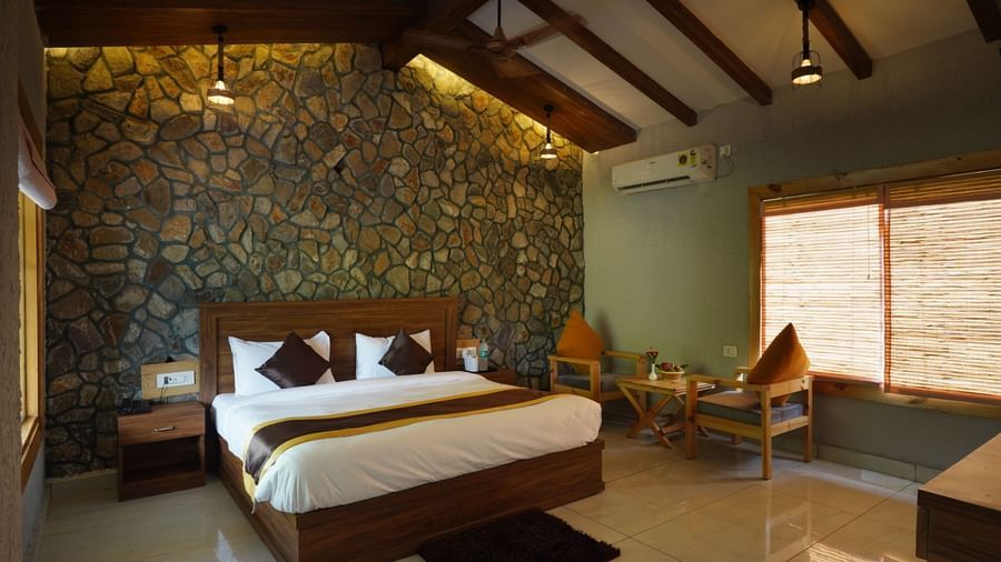 Luxury bedroom with stone accent wall, modern lighting, and double bed at Corbett Nirvana Resort.