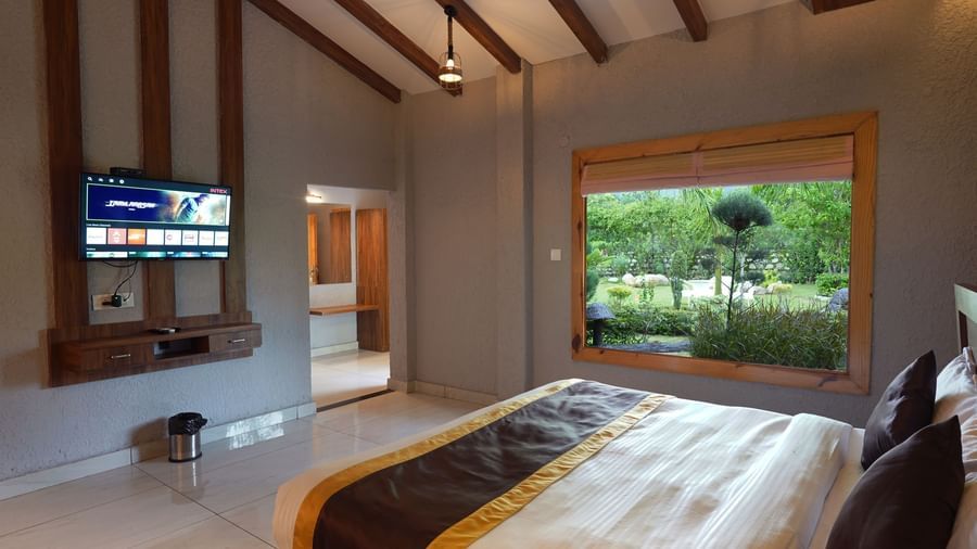 Spacious bedroom with wide window offering garden views at Corbett Nirvana Resort.